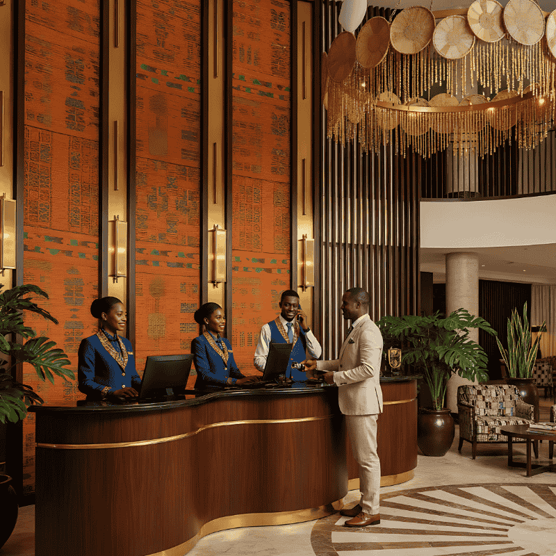 2. Front Office Staff Uniforms in Kenya A man in a light suit checks in at a hotel front desk staffed by three employees in blue hospitality front office staff uniforms in Kenya.